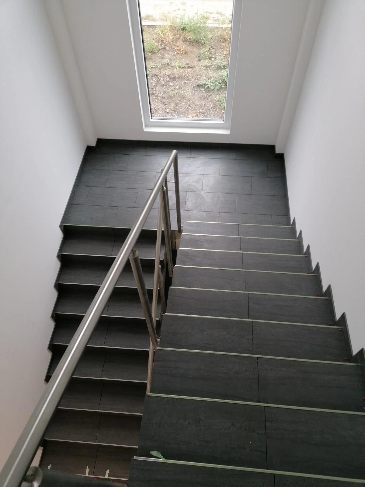 Treppenhaus mit dunklen Fliesen und Edelstahlgeländer